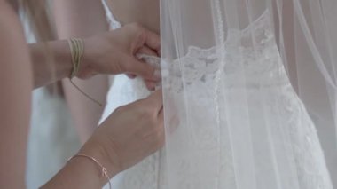 Gelinin annesi gelinliği ilikleyerek uzun peçeli kızına yardım ediyor..