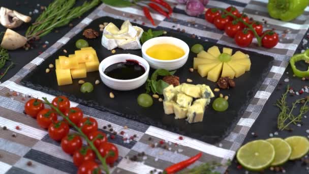 黒い石の背景においしいチーズスライスを撮影します 料理は いくつかの品種のチーズの品揃えで スライスはブラックストーンプレートと追加の装飾で提供されています — ストック動画