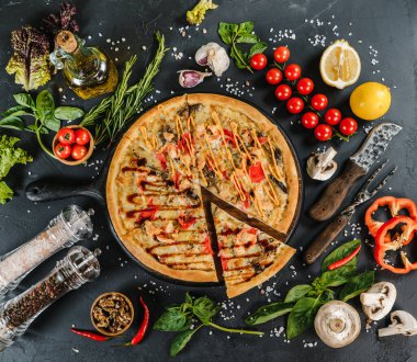 Sebze, bitki ve baharatla çevrili bir pizza.