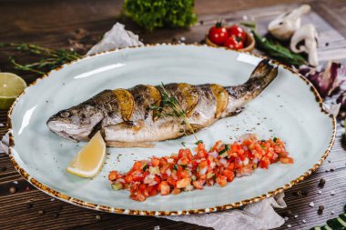 Sebze, bitki ve baharatlarla çevrili bir tabakta pişmiş balık..