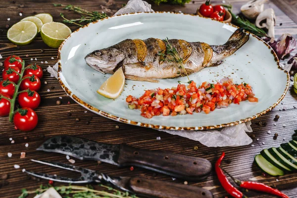 Sebze, bitki ve baharatlarla çevrili bir tabakta pişmiş balık..