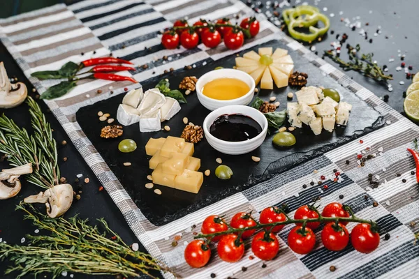 Bal, üzüm, fındık, sebze, bitki ve baharatla çevrili peynir tabağı.
