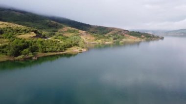 İspanya 'nın kuzeyindeki dağın zirvesinde ve adadaki gölün üzerindeki sabah sisinin hava aracı görüntüsü.