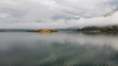 İspanya 'nın kuzeyindeki dağın zirvesinde ve adadaki gölün üzerindeki sabah sisinin hava aracı görüntüsü.