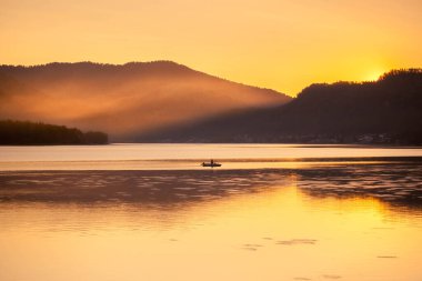 Denizde gün batımı Bir tekne ve dağlarla