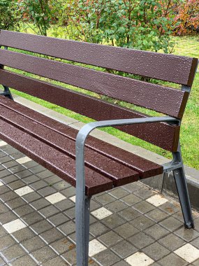 Sonbahar parkında yağmur damlaları olan ıslak boş ahşap bir bank.