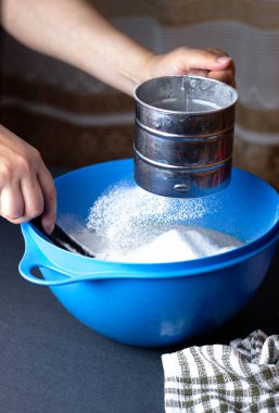 Kadın bir kase hamura un karıştırıyor.