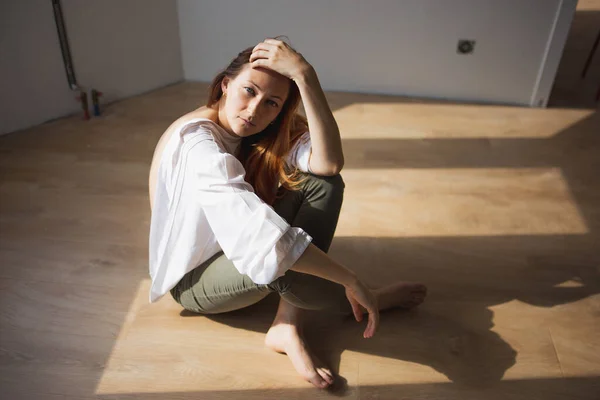 Güzel genç bir kadın yerde oturuyor ve izleyiciye bakıyor.