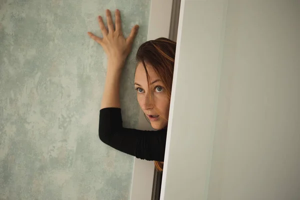 Güzel bir kadın kapının arkasından dışarı bakıyor.