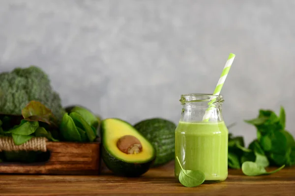 Avocado base home made green smoothies with vegetable leafy greens in a jar standing on a kitchen table, front view