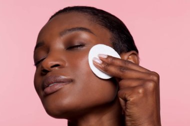 Young woman using cotton pad, studio shot 