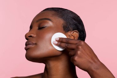 Young woman using cotton pad, studio shot 