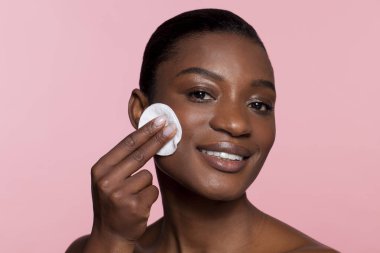 Young woman using cotton pad, studio shot 
