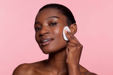 Young woman using cotton pad, studio shot 