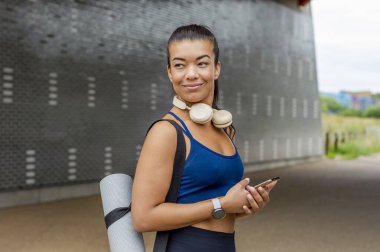 Woman with yoga mat holding smart phone