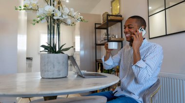 Man sitting at table, using laptop and phone