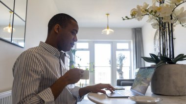Man sitting at table, using laptop and drinking coffee