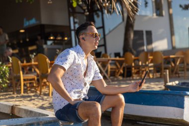 Plajda akıllı telefon kullanan kulaklık takan bir adam.