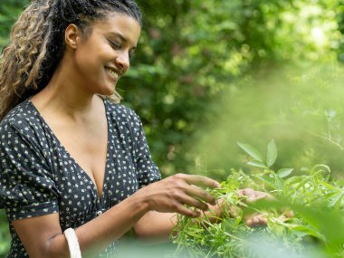 Gülümseyen kadın bitkileri sepete koyuyor.