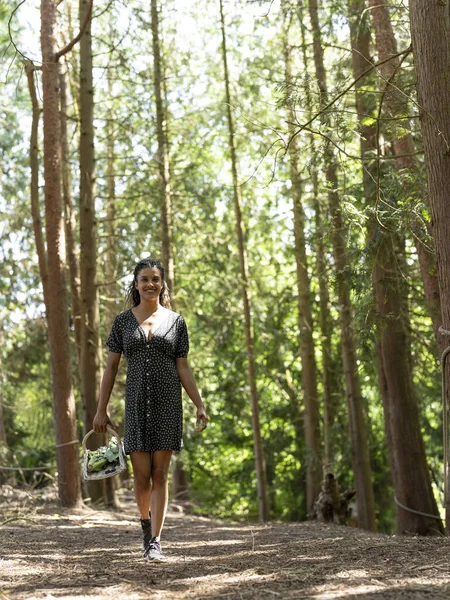 Smiling woman walking with basket in forest