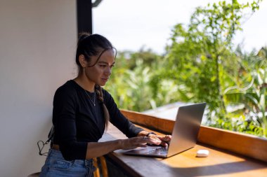 Otel odasında oturan ve dizüstü bilgisayar kullanan bir kadın.