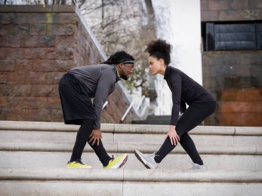Man and woman in sports clothing stretching legs on steps