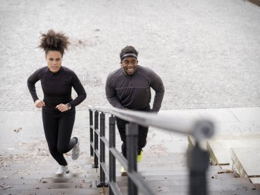 Athletic man and woman running up steps outdoors