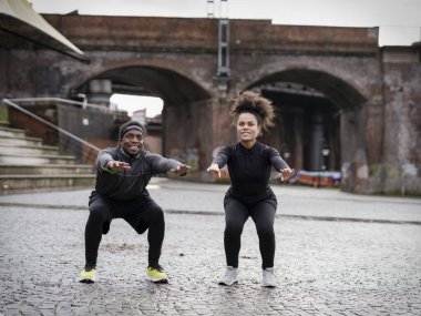 Athletic man and woman doing squats outdoors