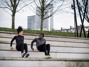 Athletic man and woman exercising on steps outdoors