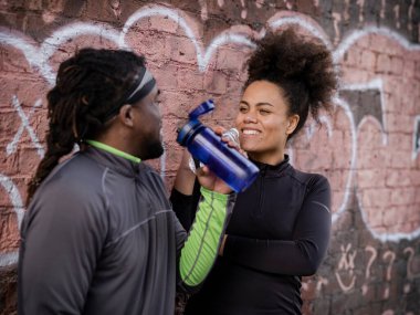 Duvarında su şişeleri olan gülümseyen atletik adam ve kadın