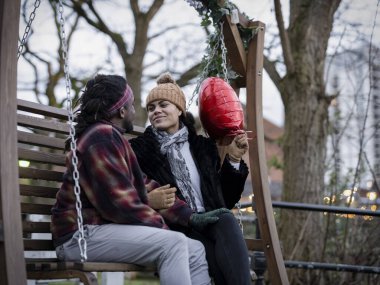 Smiling couple with heart shaped balloon sitting on swing