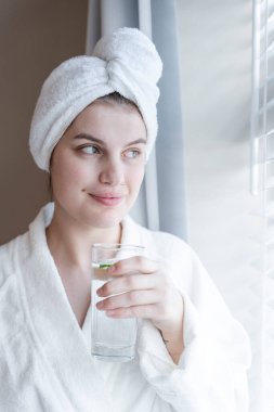 Portrait of woman in bathrobe and towel turban with glass of water