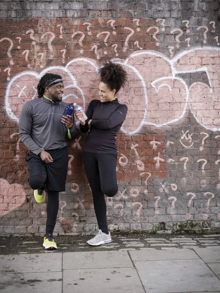 Duvarında su şişeleri olan gülümseyen atletik adam ve kadın