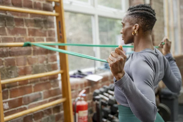 Spor salonunda direniş bandıyla egzersiz yapan atletik bir kadın.