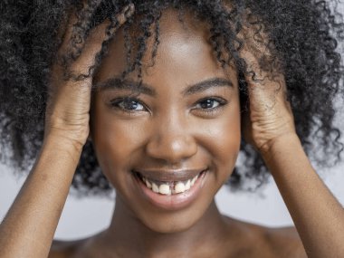 Kıvırcık saçlı, gülümseyen kadının stüdyo portresi.