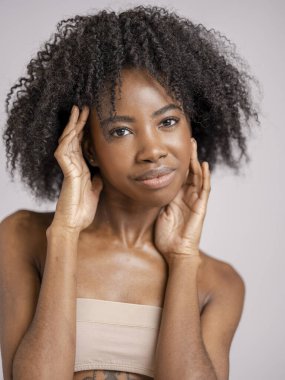 Kıvırcık saçlı, gülümseyen kadının stüdyo portresi.