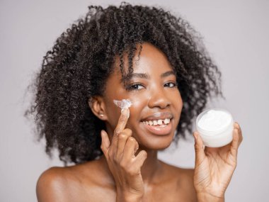 Yüz kremi sürerken gülümseyen kadının stüdyo portresi