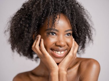 Kıvırcık saçlı, gülümseyen kadının stüdyo portresi.