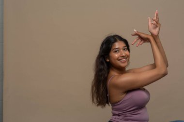 Mor bluzlu, kolları havada gülümseyen kadının stüdyo portresi.