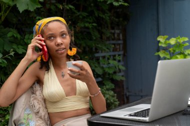 Young woman drinking tea while talking by smart phone in garden