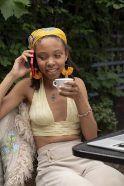 Young woman drinking tea while talking by smart phone in garden