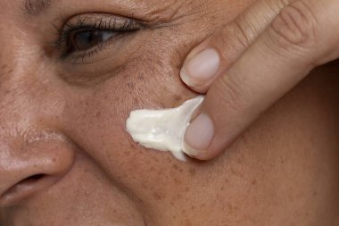 Yüz kremi süren bir kadının yakın çekimi.