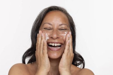 Yüz kremi sürerken gülümseyen kadının stüdyo portresi