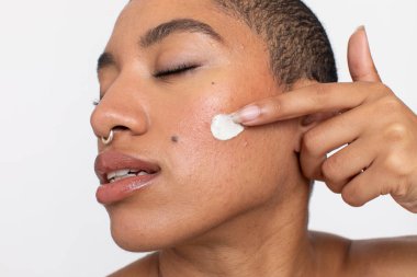 Studio portrait of woman applying face cream on cheek with eyes closed