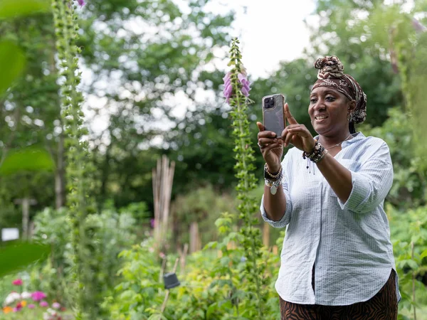 Bahçede çiçeklerin fotoğrafını çeken olgun bir kadın.