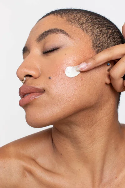 Studio portrait of woman applying face cream on cheek with eyes closed