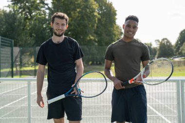 Tenis kortunda duran gülümseyen iki adamın portresi.