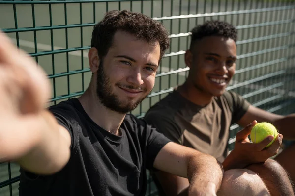 Tenis kortunda oturan iki gülümseyen adamın portresi.