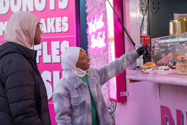 Türbanlı genç bayan turistler çörek alıyor.