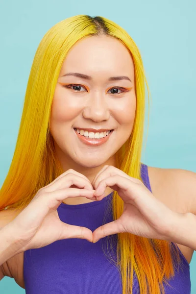 Uzun sarı saçlı gülümseyen kadının portresi, elleriyle kalbi gösteriyor.